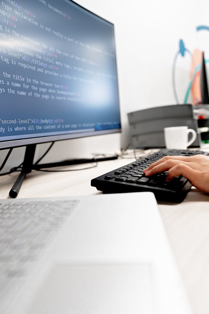 about-us Close-up of hands typing code on a computer monitor in an office setting.